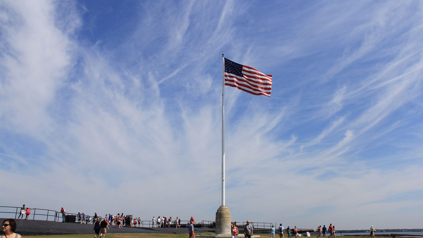 The U.S. flag flying over the parade ground at Fort Sumter with visitors along the walls
