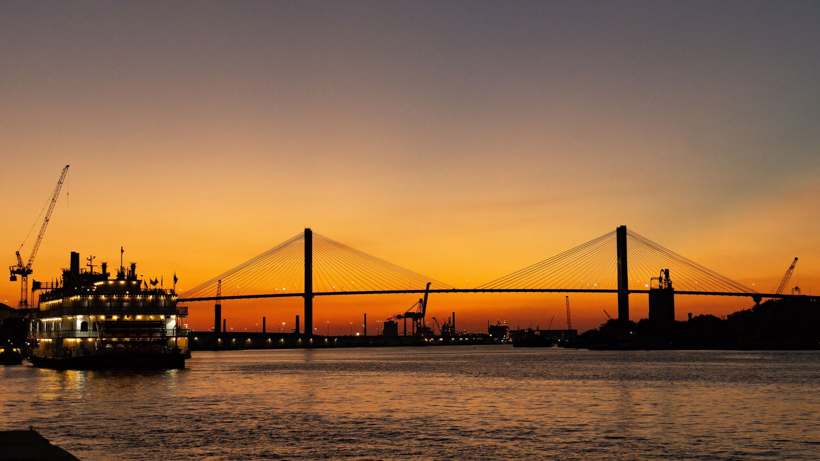 A paddle-wheel riverboat on the Savannah River at sunset with the Talmadge Memorial Bridge behind